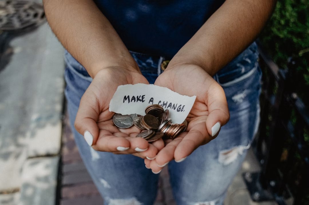 Person showing both hands with a make-a-change note and coins