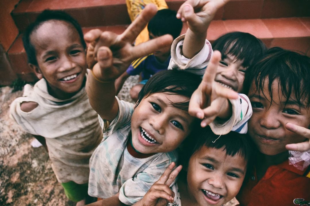 Five children smiling while doing a peace hand sign